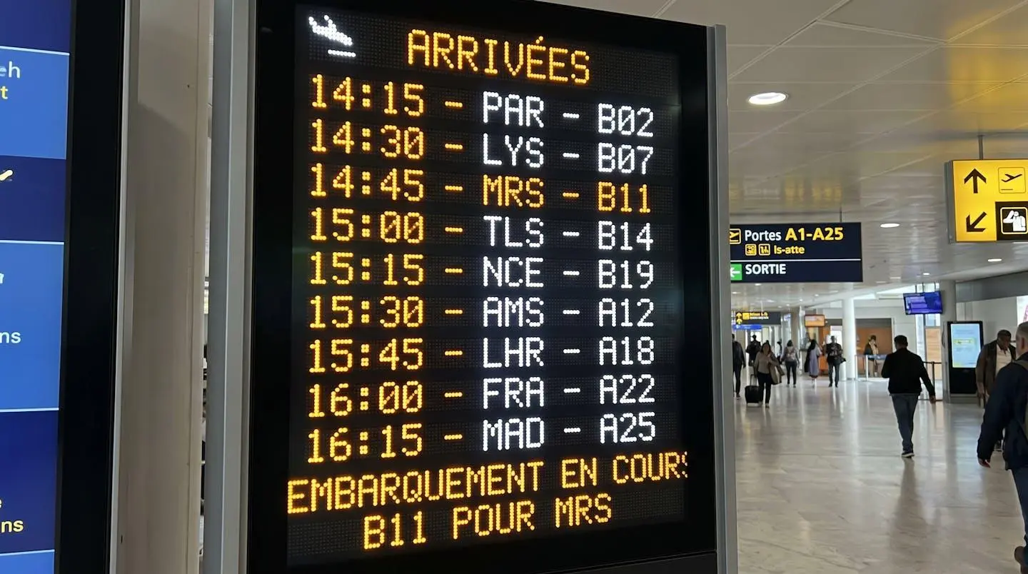 Gros plan sur un panneau d'affichage électronique montrant les horaires d'arrivée des vols et les numéros de portes dans un aéroport français